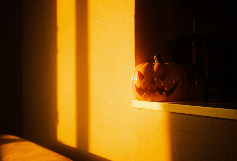 Carved Halloween pumpkin with a shadow of a window frame on the wall behind it