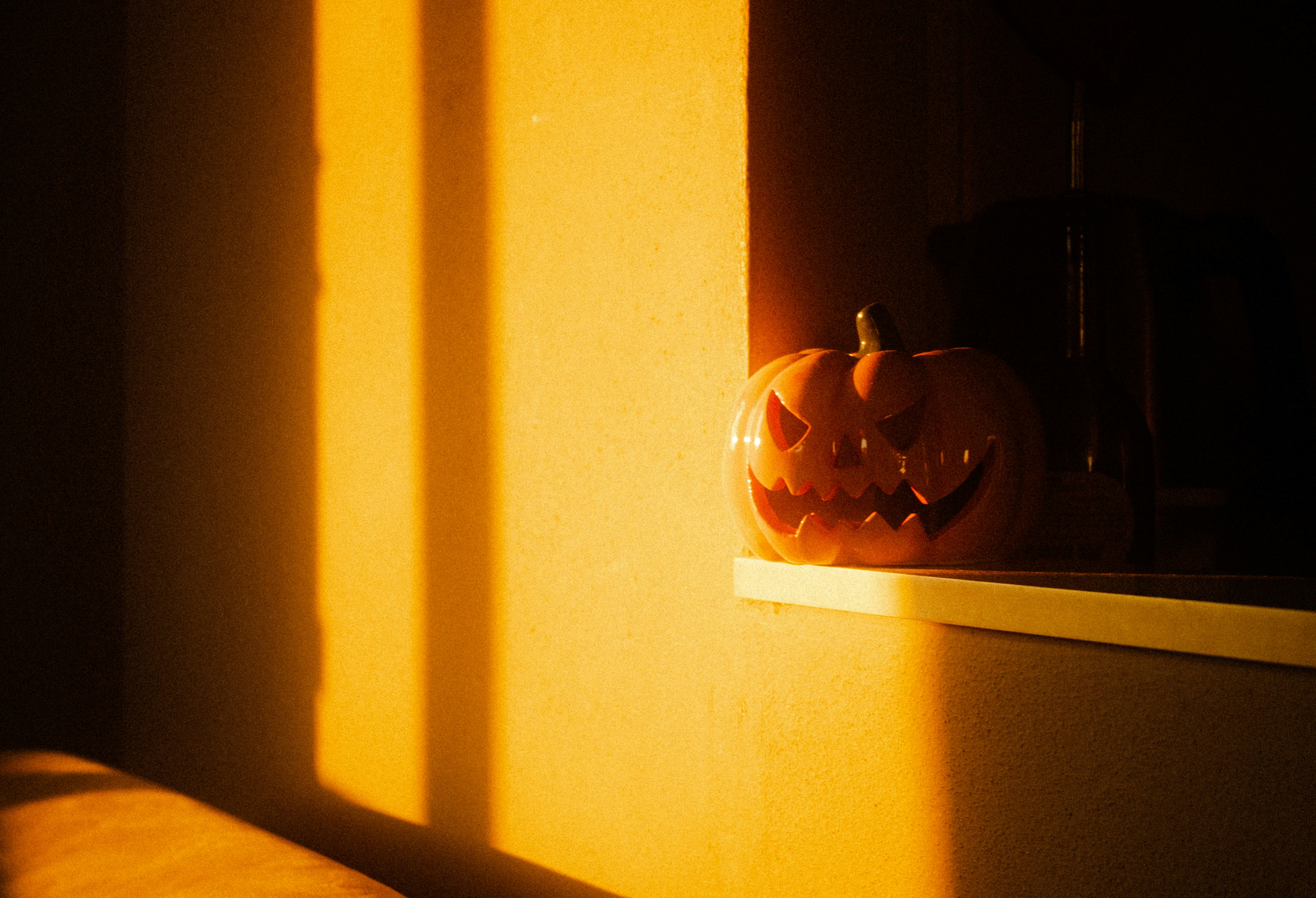 Carved Halloween pumpkin with a shadow of a window frame on the wall behind it